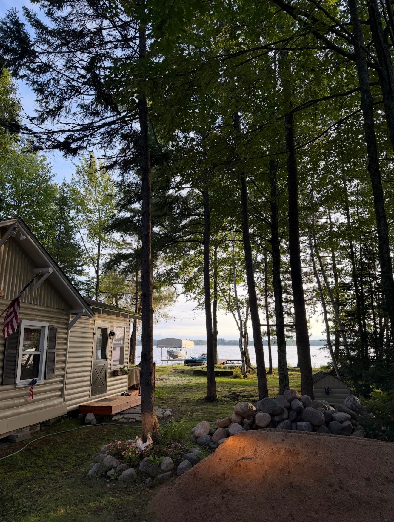 Log cabin by a lake surrounded by tall pine trees, with a boat dock in the background